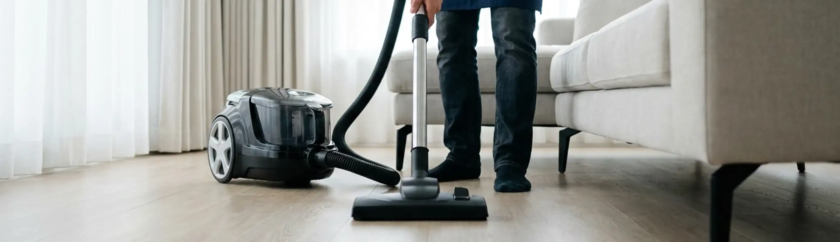 Professional house cleaner vacuuming a living room floor with a canister vacuum cleaner, Cambridge, MA.