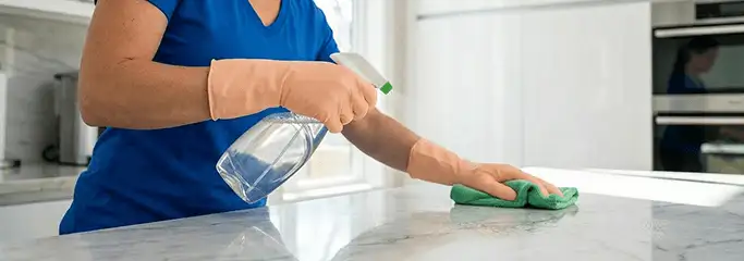 Maid service worker spraying and wiping a kitchen countertop with a microfiber cloth for sanitizing, Cambridge, MA.