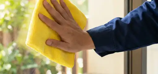 House cleaner wiping a glass window with a yellow microfiber cloth for streak-free cleaning, Cambridge, MA.